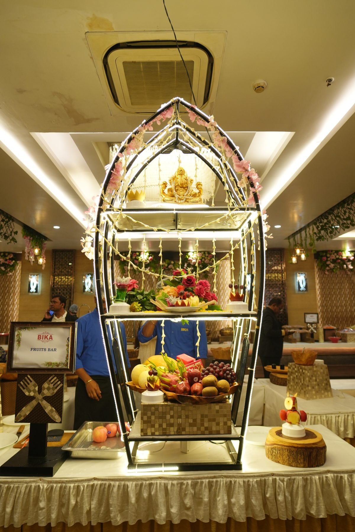 Illuminated gold boat-arch fruit and dessert buffet display at Bika Banquets, Golaghata